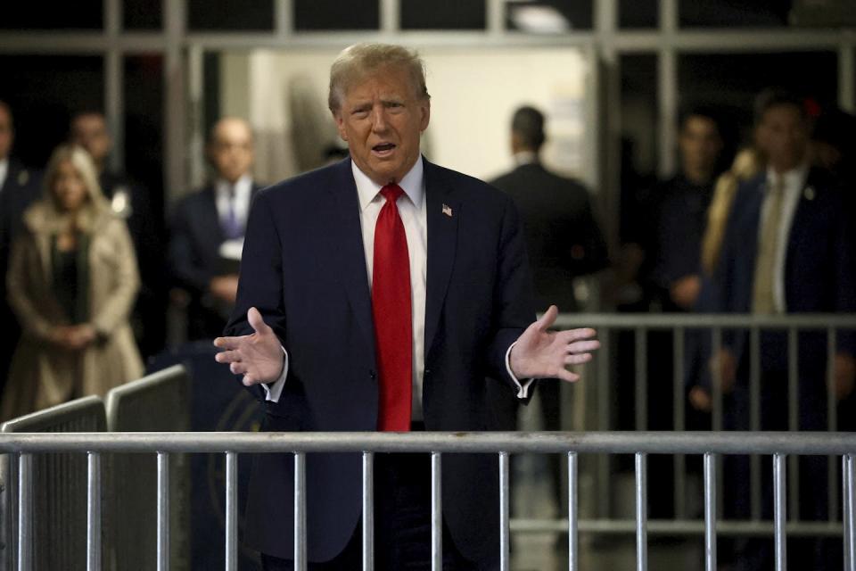 A man in a suit stands behind a fence and gestures with his hands.