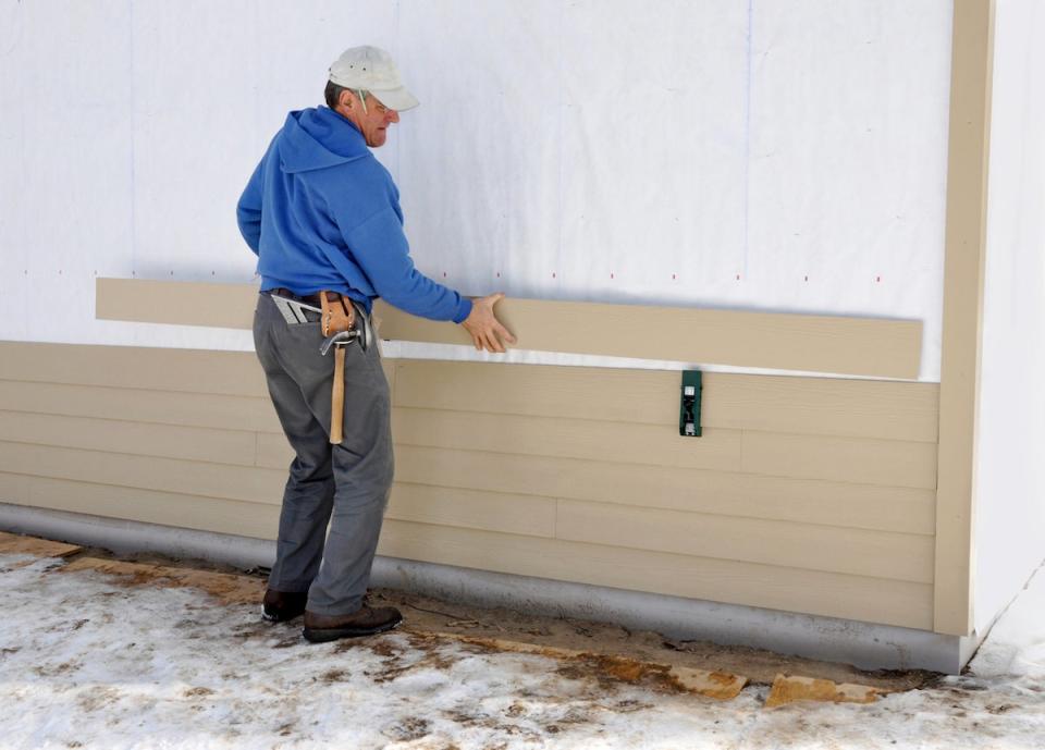 man installing fiber cement siding on house