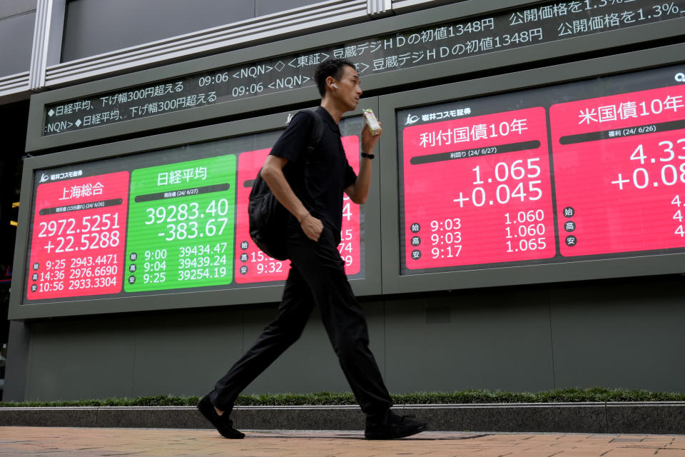 A person walks past at an electronic stock board showing financial indexes including Japan's Nikkei 225 index, green, at a securities firm Thursday, June 27, 2024 in Tokyo. (AP Photo/Shuji Kajiyama)