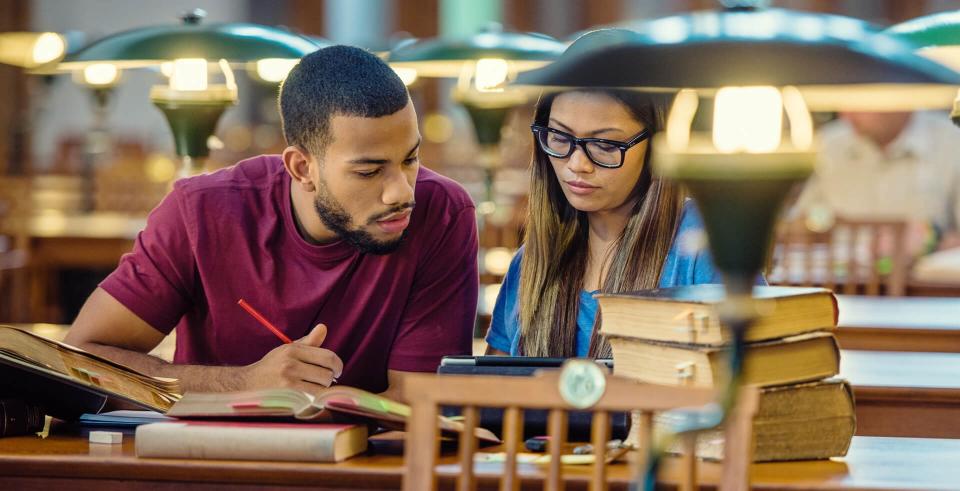 African american College student and asian girl using a digital tablet for doing research in the lecture room.