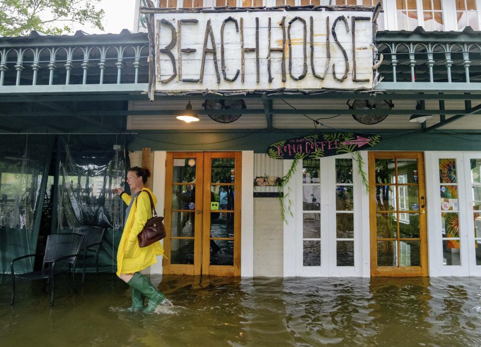 FILE - In this July 13, 2019, file photo Aimee Cutter, the owner of Beach House restaurant, walks through water surge from Lake Pontchartrain on Lakeshore Drive in Mandeville, La., ahead of Tropical Storm Barry. With earthquakes in California and Hurricane Barry striking states along the Gulf of Mexico and in the Midwest, small business owners should look at their insurance policies and determine how well covered they’d be in the event of a natural disaster. (AP Photo/Matthew Hinton, File)