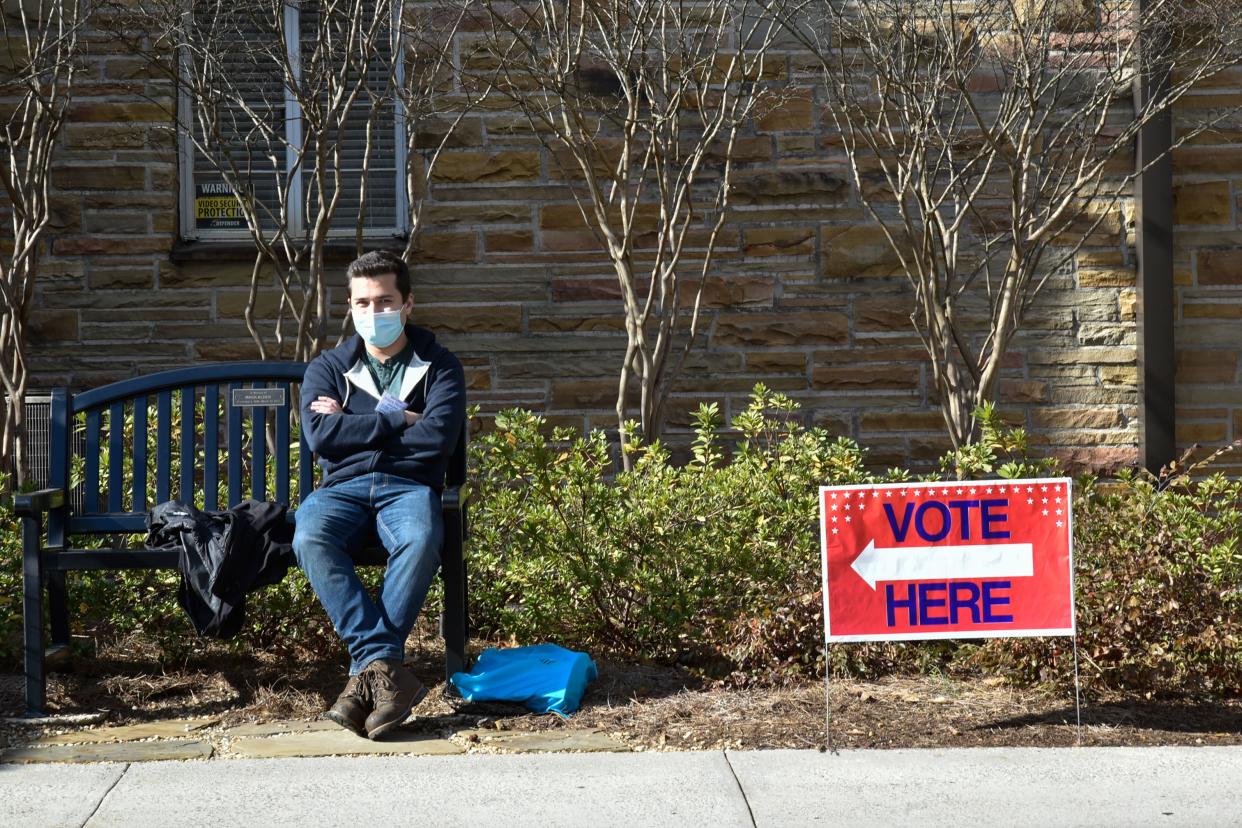 A man sits next to a vote sign 