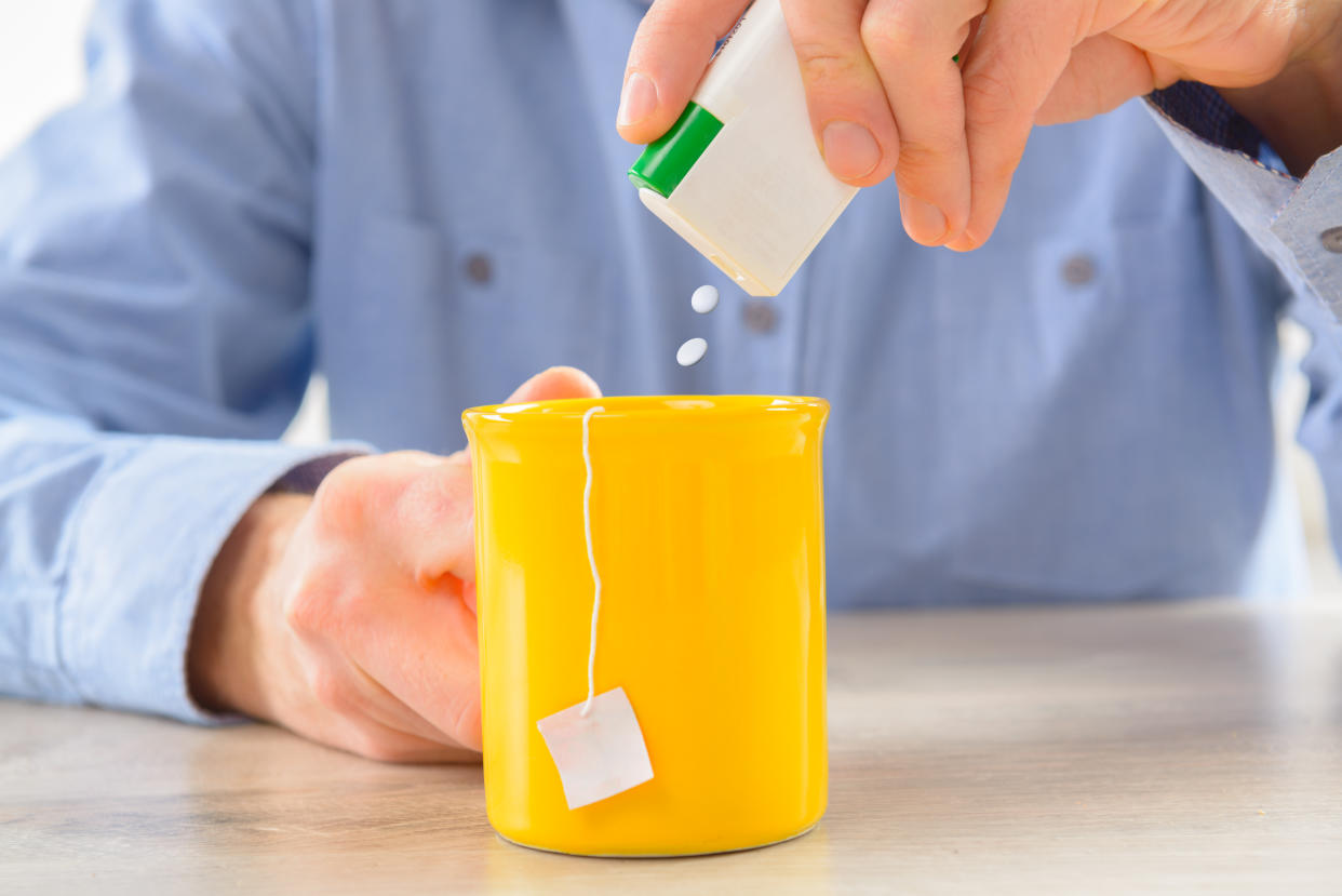 Sweetener tablets and hand with box whit cup of tea