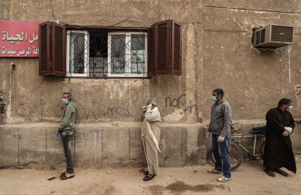 Men wearing masks wait outside an Egyptian Food Bank center in Cairo to receive cartons with foodstuffs as the charity distributes aid to people who lost their jobs due to the coronavirus pandemic. (Photo: MOHAMED EL-SHAHED/AFP via Getty Images)