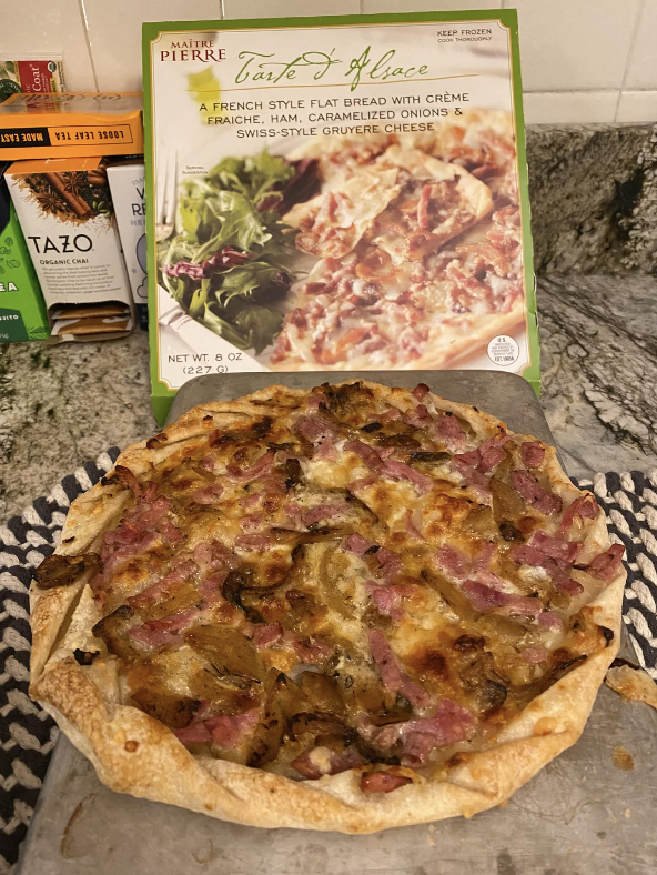 Prepared Tarte d'Alsace flatbread with ham and caramelized onions on a kitchen counter next to its packaging