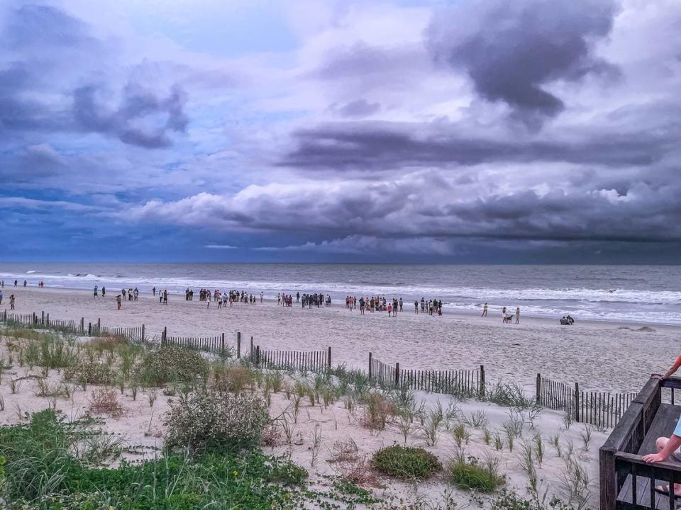 People stand on the beach in Pawleys Island as rescue crews search for a missing teen swimmer. The teen went missing in the surf Friday, July 12, 2024.
