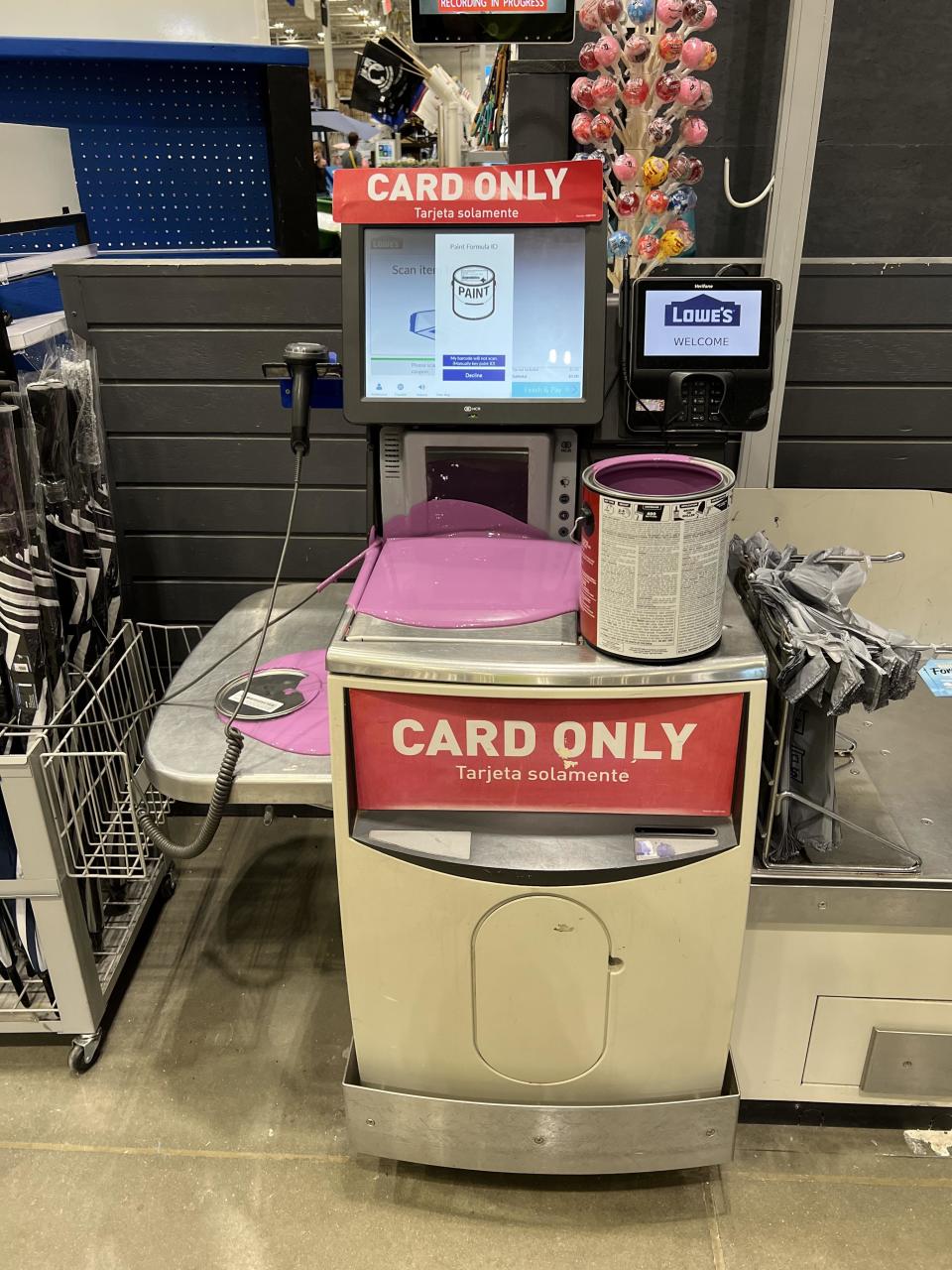 Self-checkout kiosk with "CARD ONLY" sign, screen prompts for payment, and a shopping basket with items on it