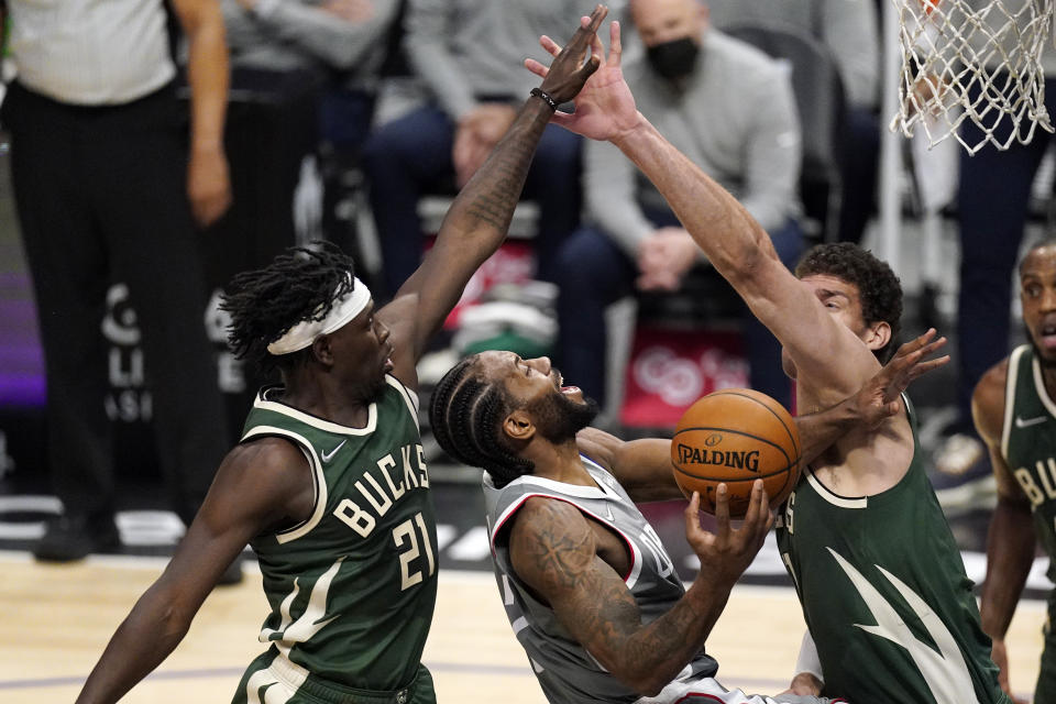 Los Angeles Clippers forward Kawhi Leonard, center, shoots as Milwaukee Bucks guard Jrue Holiday, left, and center Brook Lopez defend with their arms outstretched.