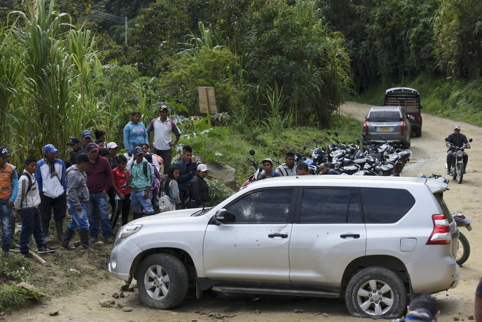 People gather around a car riddled by bullets on the road leading to Tacueyo, in southwest Colombia, Wednesday, Oct. 30, 2019. Five indigenous leaders of the Tacueyo reservation were killed late Tuesday when the two vehicles they were traveling in were ambushed by gunmen the government says are part of a dissident front of Revolutionary Armed Forces of Colombia. (AP Photo/Christian Escobar Mora)