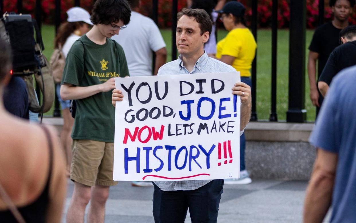 A man holds a sign reading: 'You did good, Joe! Now let's make history.'