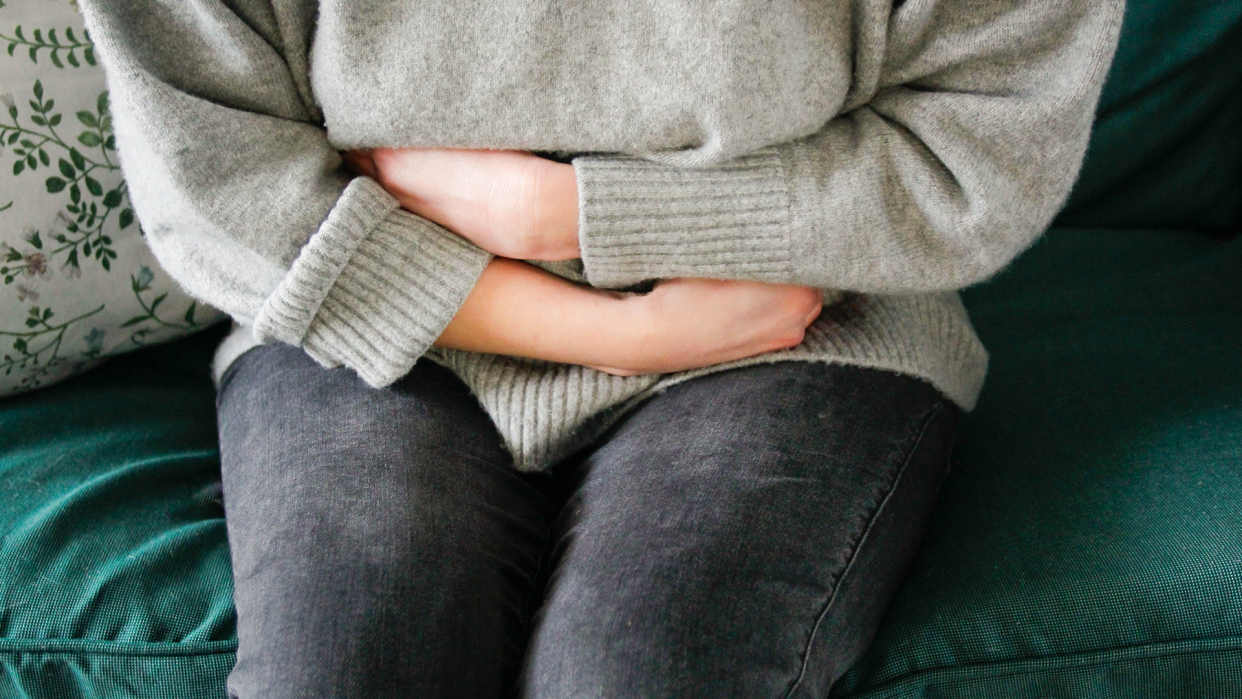 Uterine prolapse depicted as woman in sweater and jeans holding her arms around her stomach.