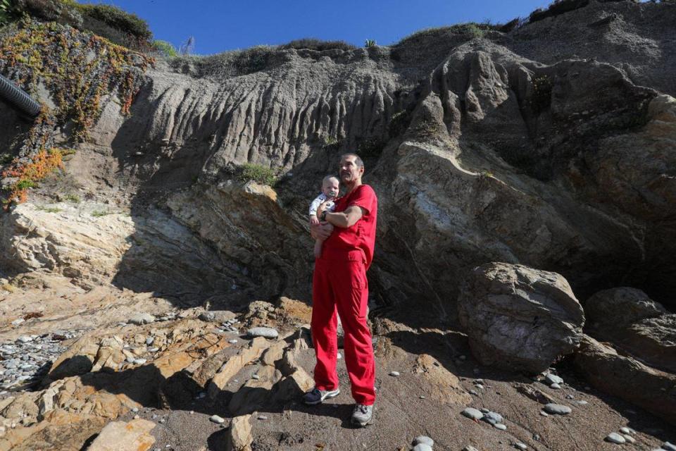 Dr. John Okerblom has been losing bluff to ocean erosion at his Pismo Beach house on Shoreline Drive. He is holding grandson Vander Sincoff Nov. 23, 2022. He has installed wells to limit water flowing through the bluff but the California Coastal Commission has denied a request to build a seawall.