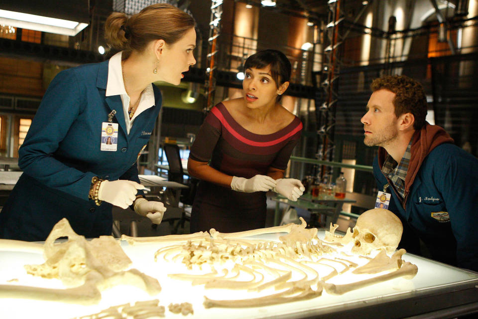 Dr. Brennan, Dr. Saroyan, and Dr. Hodgins standing around a human skeleton