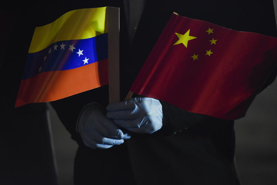 FILE - In this March 30, 2020 file photo, Venezuela's Foreign Minister Jorge Arreaza, wearing protective gloves as a preventive measure against the spread of the new coronavirus, holds a Venezuelan and Chinese flag as medical specialists and supplies arrive from China at the Simon Bolivar International Airport in La Guaira, Venezuela. While the pandemic has opened the door to much-welcomed Chinese aid in Latin America and Caribbean, it’s also made it harder for governments to pay their bills to Beijing, due to a deep recession last year wiped out nearly a decade’s worth of growth, according to International Monetary Fund data. (AP Photo/Matias Delacroix, File)