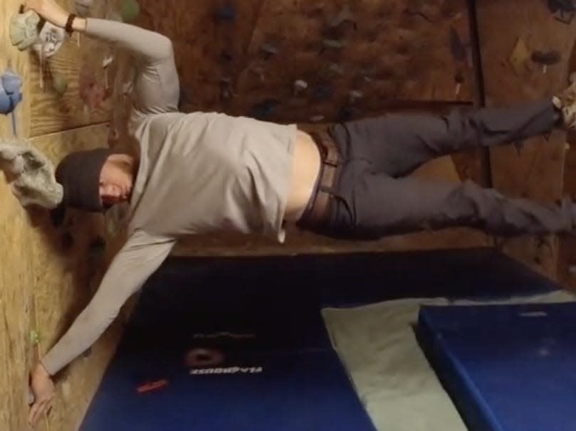 A male member of staff at the Amundsen-Scott south Pole station is hanging horizontally from a climbing wall made of plywood.