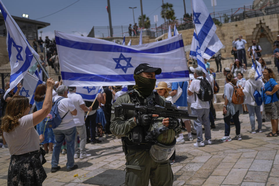 An Israeli police officer stands guard as Israelis wave national flags ahead of a march marking Jerusalem Day, an Israeli holiday celebrating the capture of east Jerusalem in the 1967 Mideast war, in front of the Damascus Gate of Jerusalem's Old City, Thursday, May 18, 2023. (AP Photo/Ohad Zwigenberg)