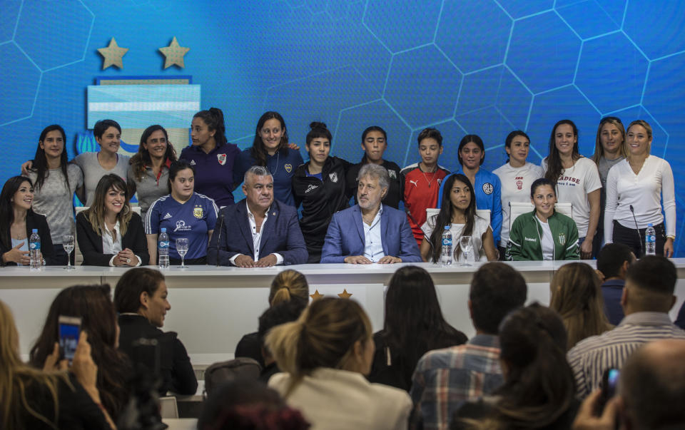 Accompanied by soccer players, Claudio Tapia, president of Argentina's Soccer Federation, bottom center, and General Secretary of the Argentina's Footballers' Union (FAA) Sergio Marchi, bottom, second from right, pose for pictures during a press conference to announce the early implementation of a plan to professionalize women's soccer in Buenos Aires, Argentina, Saturday, March 16, 2019. Almost 90 years after men's soccer turned professional in Argentina, the women's game is still being played by amateur athletes who get little to no money for their work on the field. (AP Photo/Daniel Jayo)