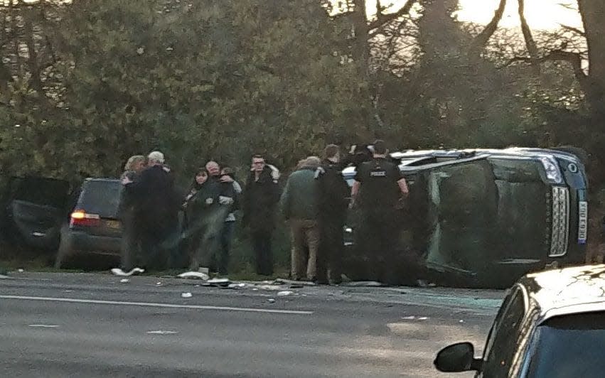 The scene of Prince Philip's car crash. He is in the centre, wearing a green jacket, and his Land Rover is seen on its side