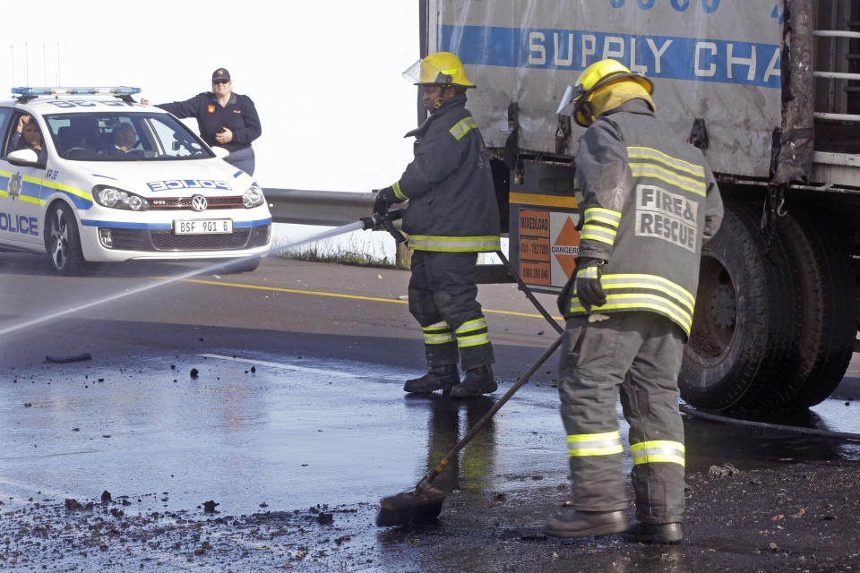 Firemen clear debris and fuel from the road, as Police provide security, left, after a truck was set alight by striking truck workers on a slipway off a main highway leading out of the city, near the international airport in Cape Town, South Africa, Friday, Oct 5, 2012. South African truck workers have been on strike for two weeks over wages, with sporadic violence reported and a number of trucks being set alight in past days. (AP Photo/Schalk van Zuydam)