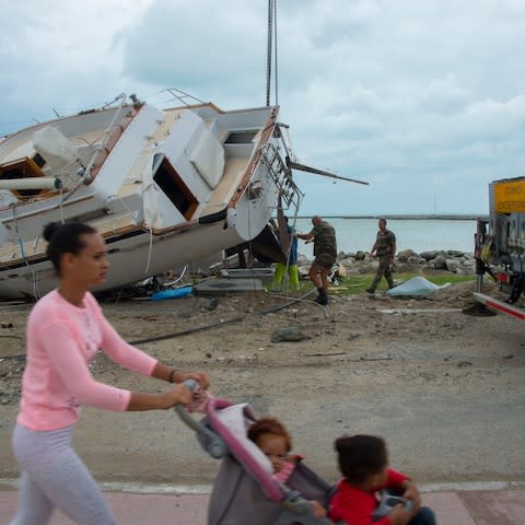 A woman pushes her kids as members of the military help remove damaged boats after the passage of hurricane Irma and Maria in Orient Bay, St. Martin - Credit: HELENE VALENZUELA/AFP/Getty Images