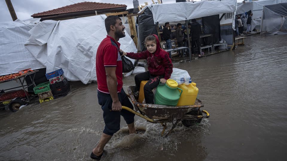 A man carries his daughter in a wheelbarrow through the flooded streets of a UN displacement camp in Khan Younis, in southern Gaza, on November 19. Infectious diseases including diarrhea, jaundice, acute hepatitis and respiratory infections are spreading in the strip. - Fatima Shbair/AP