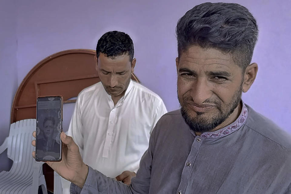 Raja Sakundar, right, holds up a picture of his nephew on his phone, who is missing after a shipwreck off the Greek coast, in Bindian village in Kotli, a district of Pakistan's administrator Kashmir, Sunday, June 18, 2023. Pakistani Prime Minister Shehbaz Sharif declared a national day of mourning for citizens who died when the fishing trawler packed with migrants they were in sank off the Greek coast. (AP Photo/Nasir Mehmood)