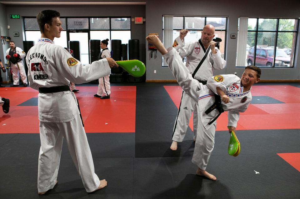 Fifth degree Black Belt and instructor owner Michael Poole (middle in background) watches as Jaxon Lowry, 10 of Lancaster, practices his kicks as Liam Kinder, 16 of Carroll, holds a target for him to kick inside of the Lancaster ATA Martial Arts on July 31, 2023, in Lancaster, Ohio. The Taekwondo students, along with instructor Michael Poole, went to the ATA World Championships in Phoenix, Arizona where Kinder took third in traditional sparring, and Evelyn Hill (not shown), 16, took first place in extreme weapons. Lowry did not place in worlds but won first place in traditional sparring and combat at the state level championship.