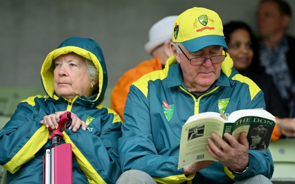 A fan of Australia reads a book, about Don Bradman, during the rain delay prior to Day Fi