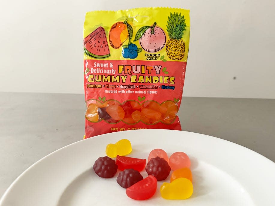 Orange and yellow bag of Trader Jpe's fruity gummy candies with candies shaped like blackberries, watermelon, pineapple, and oranges in front of bag