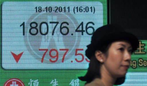 A woman walks past a display board showing the Hang Seng stock market index in Hong Kong, 2011. Asian markets fell and the euro sat near multi-year lows amid growing fears that Spain will need a full bailout, while tech shares were hit by Apple's disappointing earnings report
