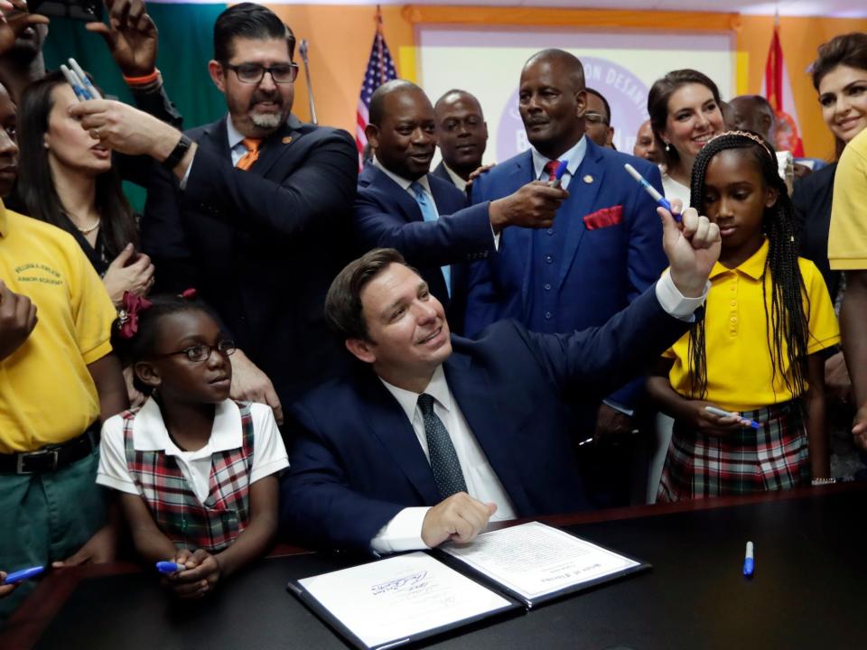 Florida Gov. Ron DeSantis, center, passes out pens used to sign a bill during a signing ceremony at the William J. Kirlew Junior Academy, Thursday, May 9, 2019, in Miami Gardens, Florida.