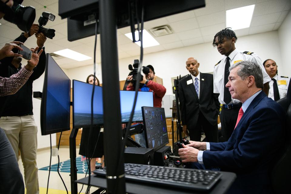Gov. Roy Cooper tries his hand at the flight simulator while members of the media photograph him during a tour of E.E. Smith High School on Tuesday, Feb. 27, 2024.