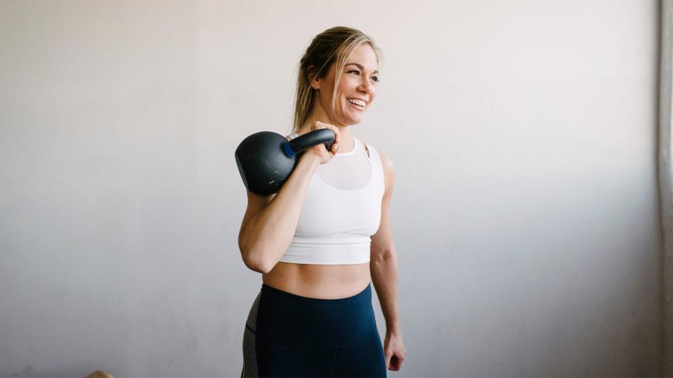 Woman holding kettlebell above her shoulder, smiling and laughing in workout clothes