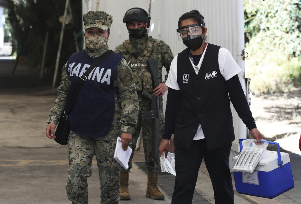 A health worker is escorted by soldiers as she arrives to the Sports Center with a cooler containing doses of the Russian COVID-19 vaccine Sputnik V, for a mass vaccination campaign against the new coronavirus for the elderly in the Xochimilco borough of Mexico City, Wednesday, Feb. 24, 2021. (AP Photo/Marco Ugarte)