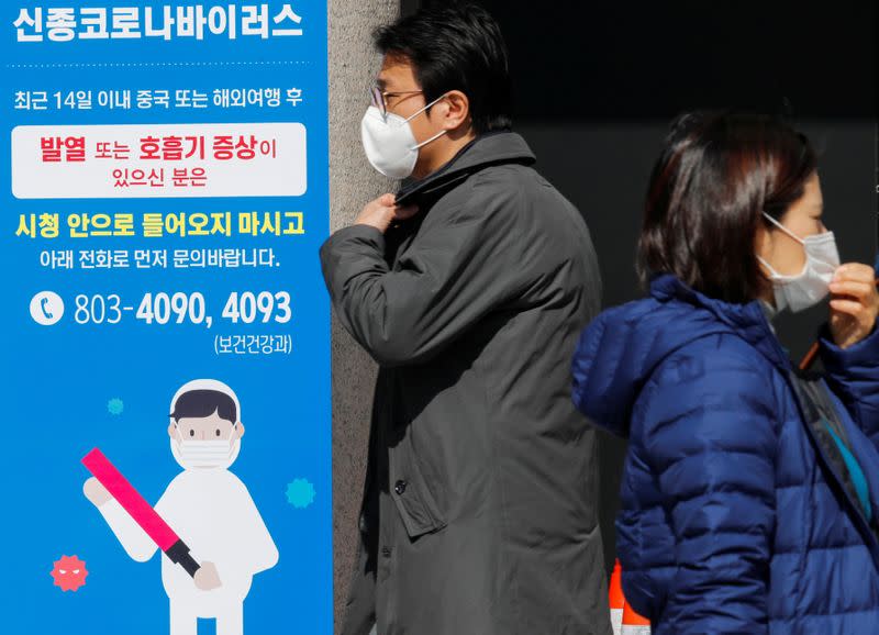 People wearing protective masks walk past a notice about the novel coronavirus disease of COVID-19 in front of the city hall in Daegu