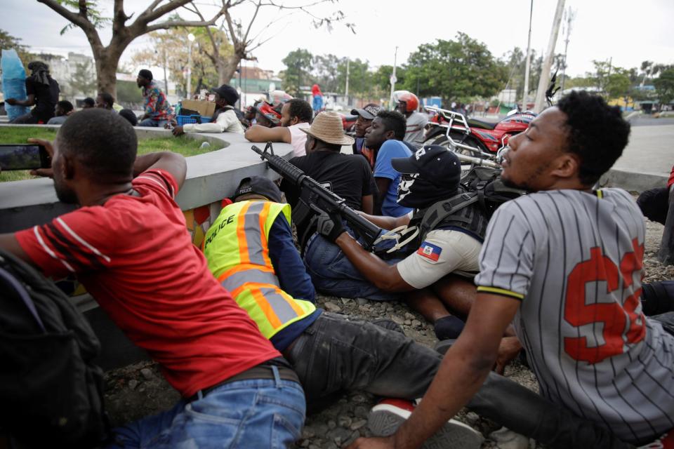 A man in a Haitian National Police uniform aims a rifle as people take cover during a shooting in Champ de Mars, Port-au-Prince, Haiti February 23, 2020.