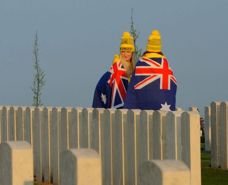 People wrapped in Australian flags walk past graves at the Australian War Memorial in the northern French city of Villers-Bretonneux, on April 25, 2013. Tens of thousands of Australians and New Zealanders turned out Thursday to honour their war dead, with moving tributes to fallen mates and calls not to forget those injured in conflict