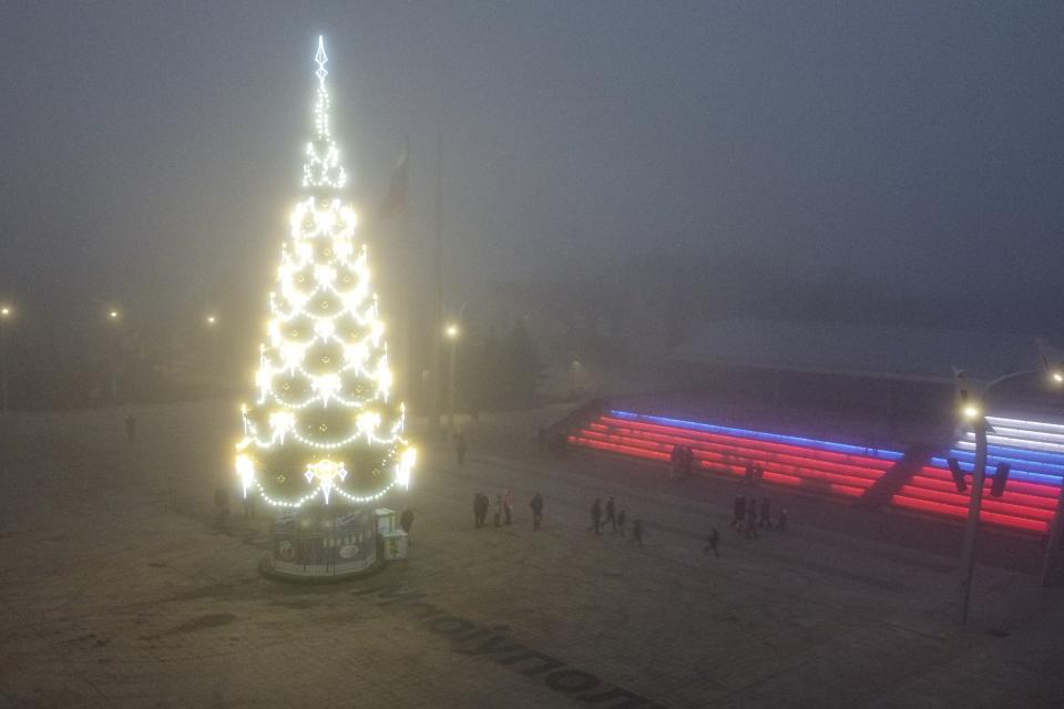 People walk past a Christmas tree decorated for Christmas and the New Year festivities in Mariupol, in Russian-controlled Donetsk region, eastern Ukraine, Saturday, Dec. 24, 2022. (AP Photo)