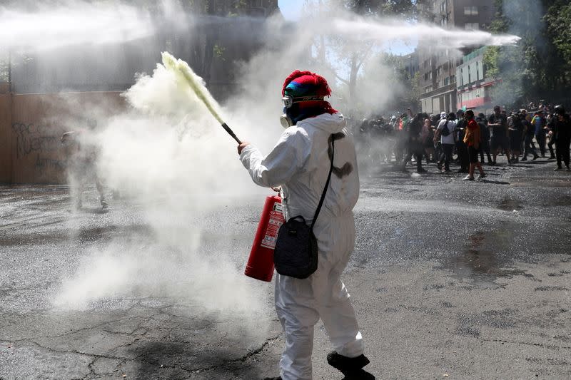 Un manifestante utiliza un extintor de fuego mientras la policía utiliza el carro lanzaaguas para dispersar a las personas durante el primer aniversario de las masivas protestas contra el gobierno, en Santiago, Chile