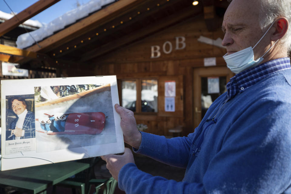 Renzo Costantini shows a picture of American bobsledder James Morgan who died in a crash on the track during the 1981 world championships, in Cortina d'Ampezzo, Italy, Wednesday, Feb. 17, 2021. Costantini pines for the good old days when drivers and brakemen would come whizzing down the track on one side of the café and then hop off their sleds on the other side and come in for a shot of espresso, a vin brulé or perhaps even a taste of the local grappa. (AP Photo/Gabriele Facciotti)