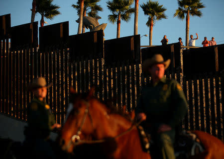 FILE PHOTO: People in Mexico wave at U.S. Border Patrol agents on horseback patrolling the U.S.-Mexico border fence near San Diego, California, U.S., November 10, 2016. REUTERS/Mike Blake/File Photo