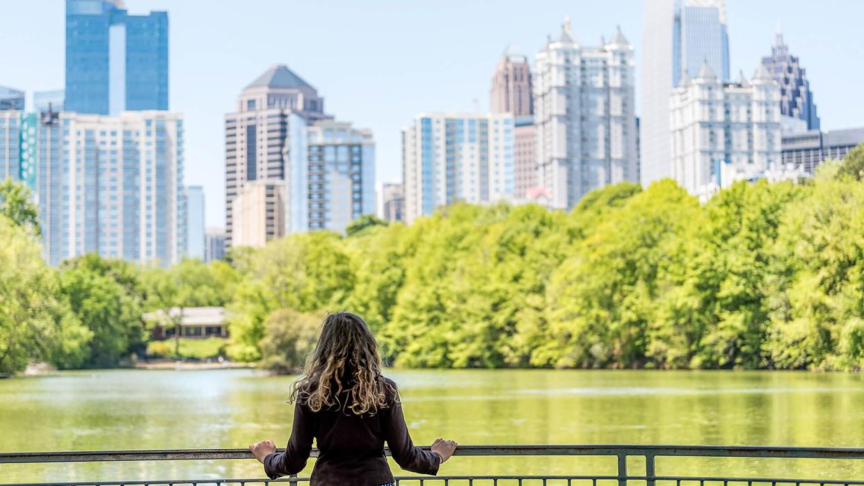 Young woman standing in Piedmont Park in Atlanta, Georgia looking at scenic water, and cityscape skyline of urban city skyscrapers downtown, Lake Clara Meer.