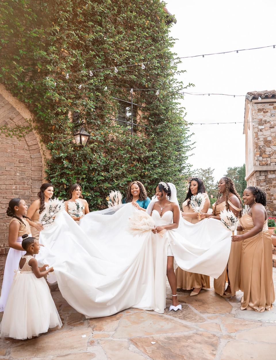 A bride stands with her bridesmaids as they adjust her dress.