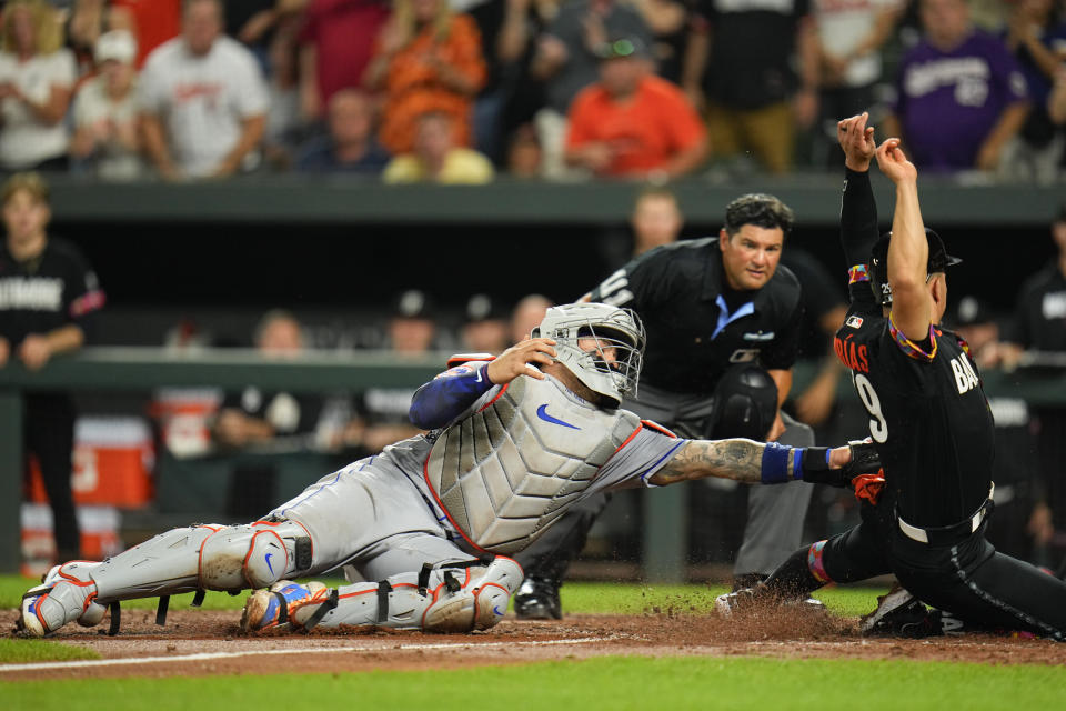 New York Mets catcher Francisco Alvarez, left, attempts a tag on Baltimore Orioles' Ramon Urias as he scores on a two-run double by James McCann in the sixth inning of a baseball game, Friday, Aug. 4, 2023, in Baltimore. Orioles' Colton Cowser also scored on the double. (AP Photo/Julio Cortez)