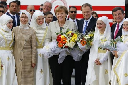 German Chancellor Angela Merkel (C), EU Council President Donald Tusk and Turkish Prime Minister Ahmet Davutoglu (R) pose with flowers during a welcoming ceremony at Nizip refugee camp near Gaziantep, Turkey, April 23, 2016. REUTERS/Umit Bektas