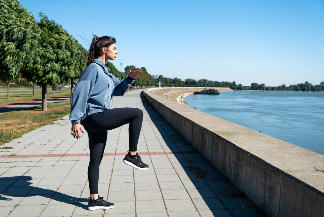 A woman in workout clothes exercising in a park doing knee raise single leg balance movement.