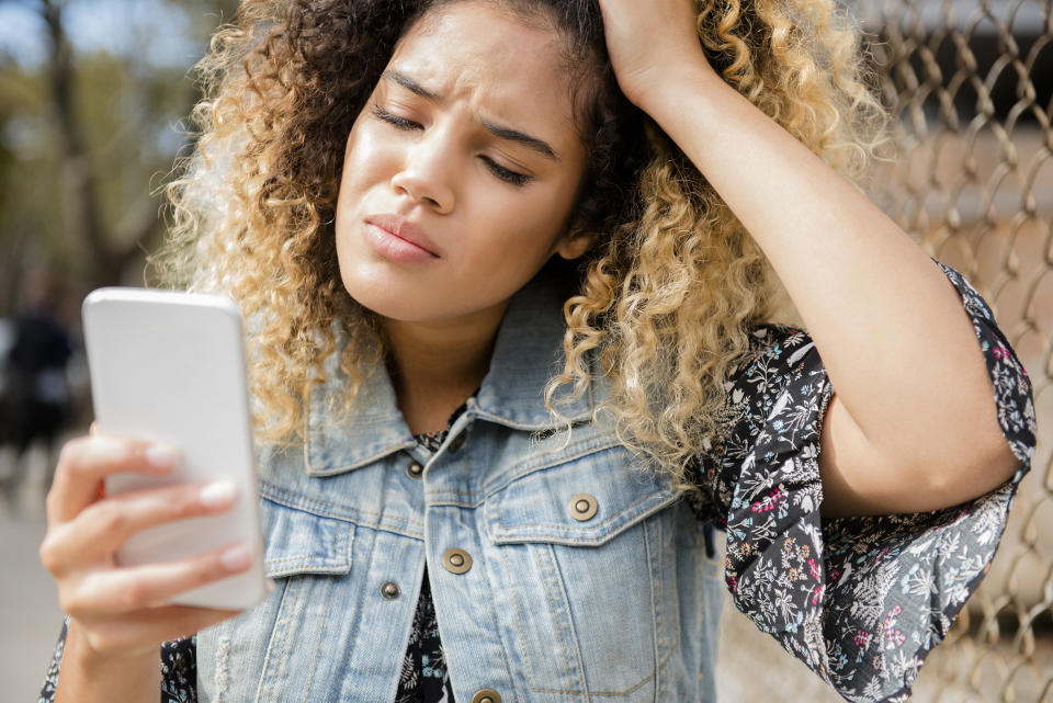 Unhappy Mixed Race woman texting on cell phone (Jamie Grill / Getty Images stock)