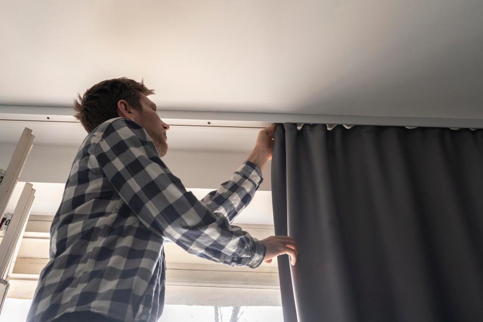 Man hanging grey curtains on window