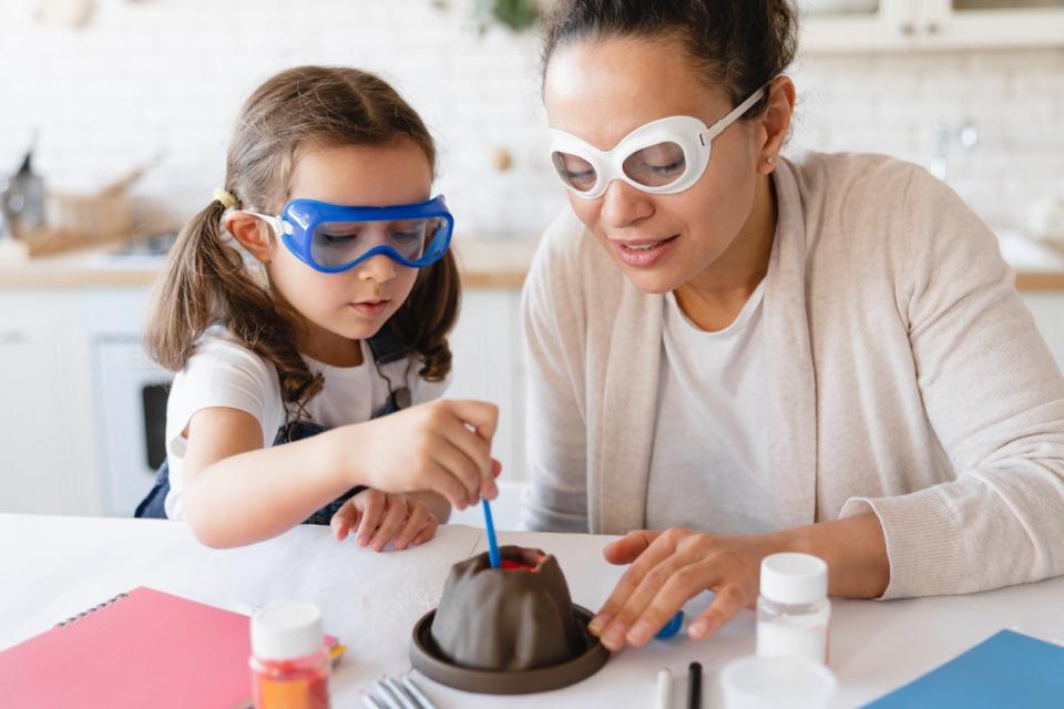 Young mother helping her daughter with science experiment with volcano eruption at home kitchen. Chemistry lab at home. Baking soda for project