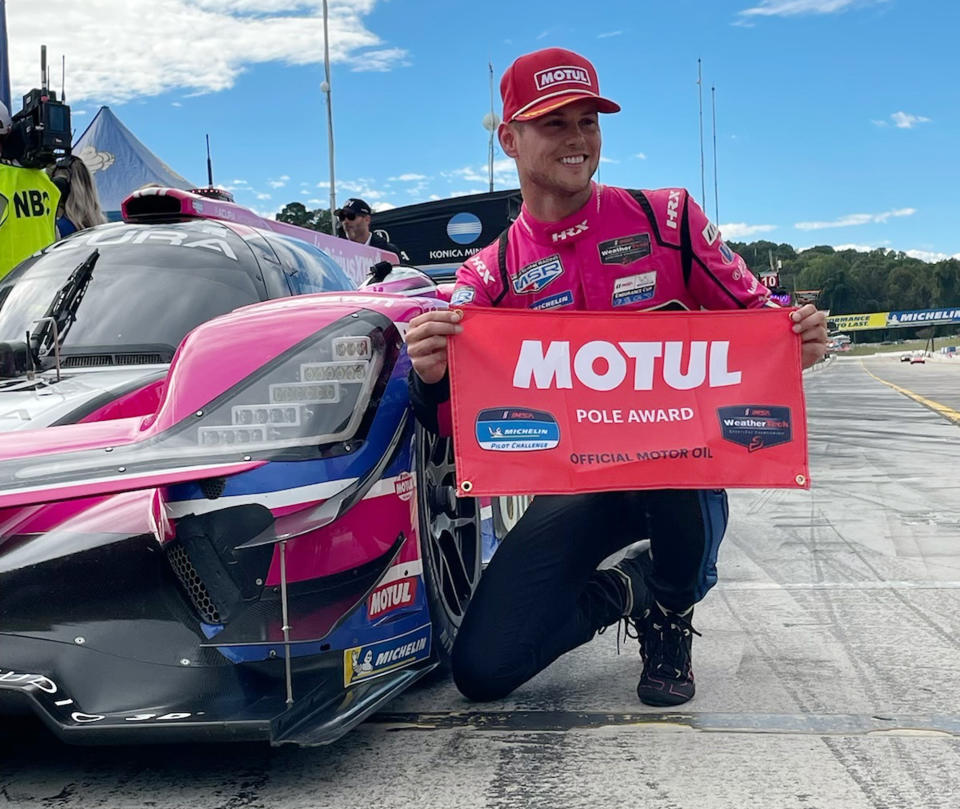 Tom Blomqvist, of Meyer Shank Racing, poses with flag after qualifying for the pole position, Friday, Sept. 30, 2022, in the IMSA sports cars season-ending Petit Le Mans auto race at Road Atlanta in Braselton, Ga. The team goes into Saturday's race second in the championship standings. Ensuing pictures show teammate Helio Castroneves congratulating Blomqvist, team owner Mike Shank and drivers Helio Castroneves and Oliver Jarvis watching Blomqvist qualify. (AP Photo/Jenna Fryer)